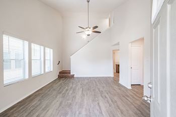 An empty living room with white walls and a ceiling fan